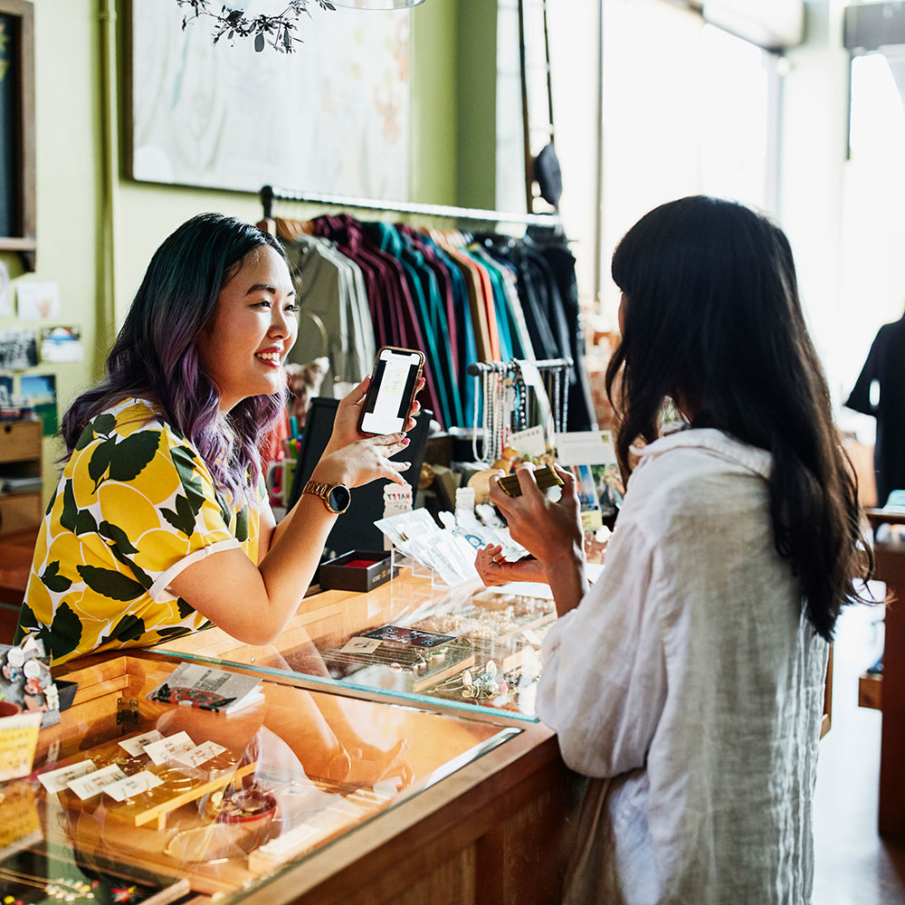 Woman displaying an item on a cell phone to a shop patron