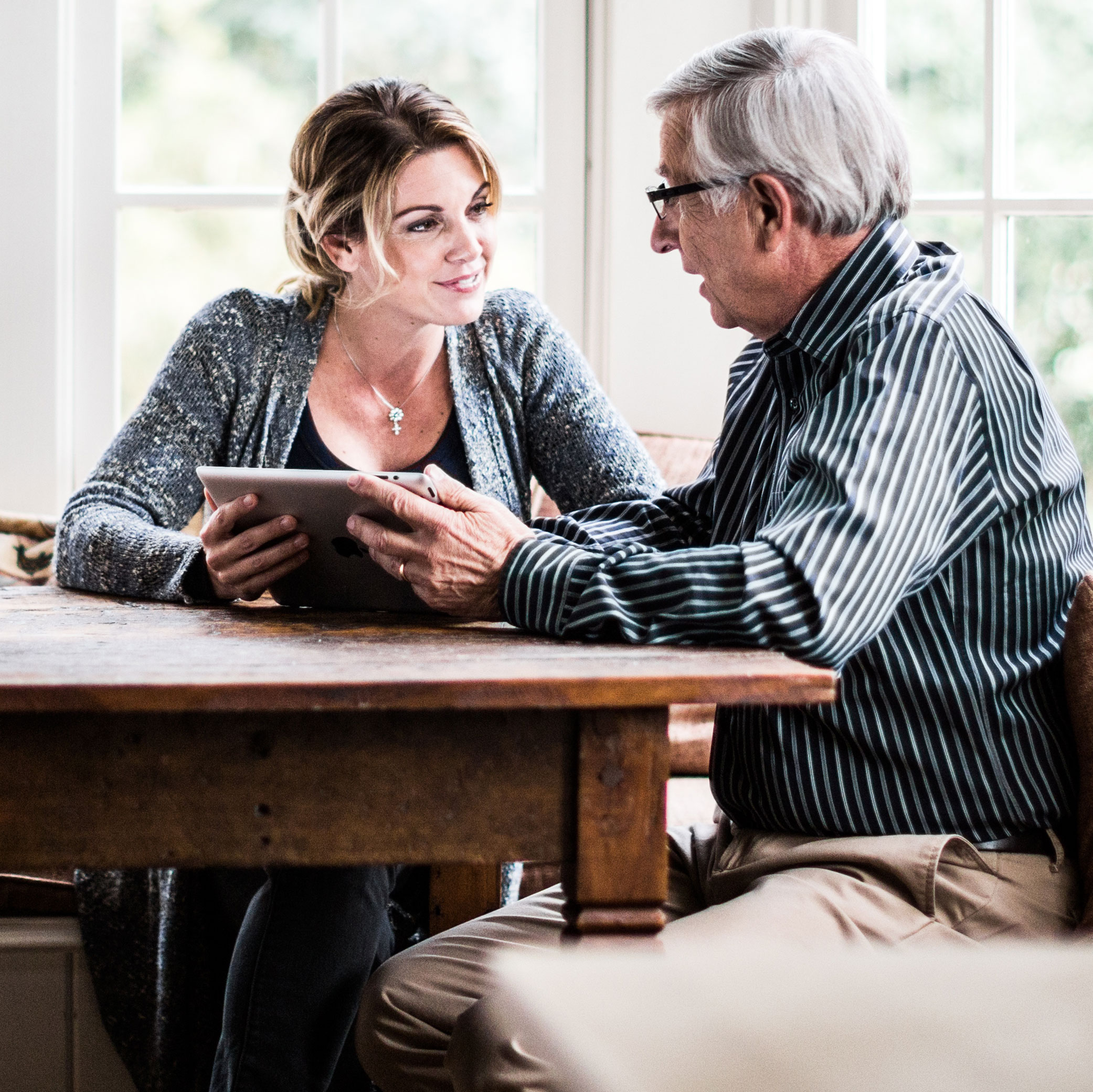 Woman speaks to older man at kitchen table with a tablet device