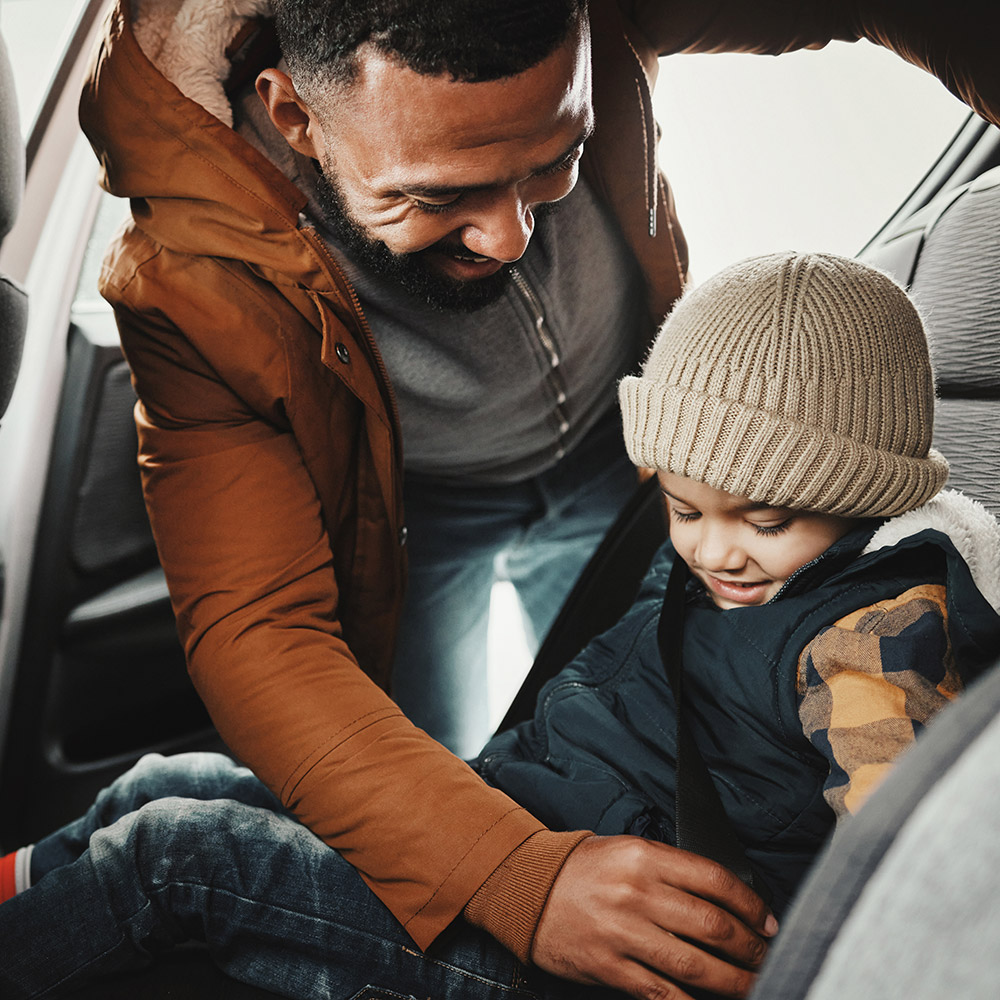 dad buckling up child in car seat