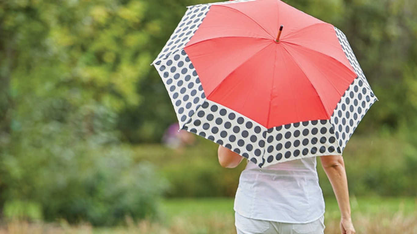 A person holding a pink umbrella and walking in a garden.