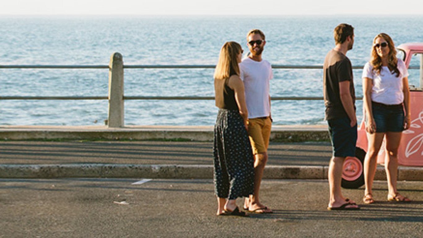 Four people standing near the ocean and ordering sweets from the pink food truck.