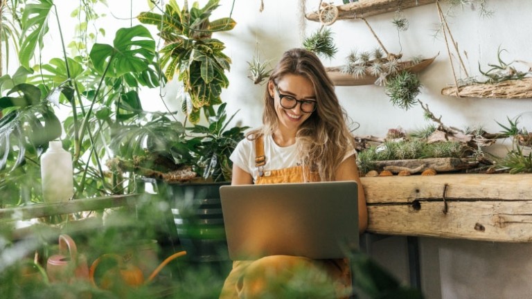 Woman plant shop business owner with glasses and hair down viewing laptop.