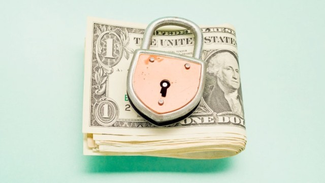 Dollar bills folded underneath copper lock on pale green background