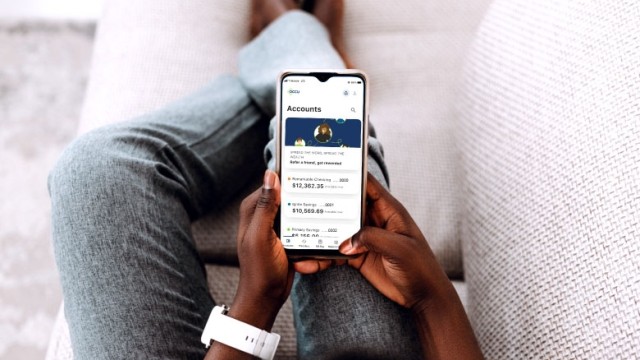 Person on couch viewing financial account information on mobile phone app.