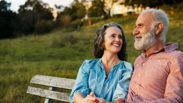 Retiree couple sitting on a park bench peacefully during golden hour in a park.    
