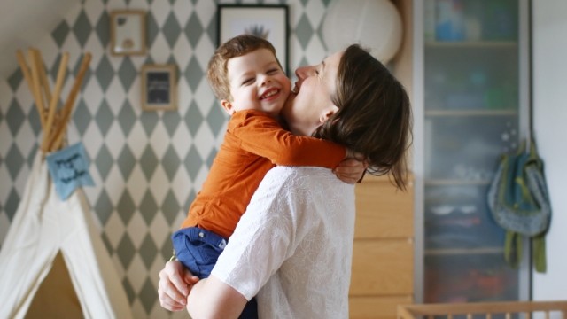 Mother and toddler hugging in home nursery with smiles.