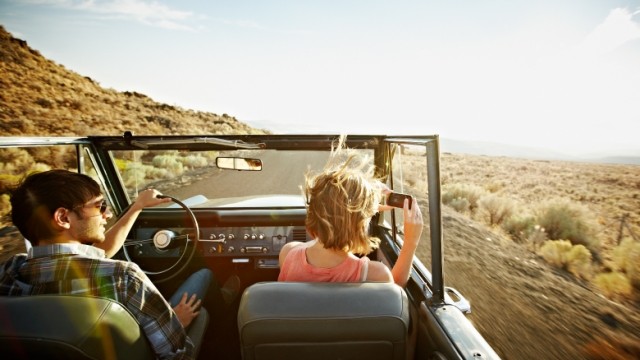 Couple driving on the open road in an old convertible car and taking photos.