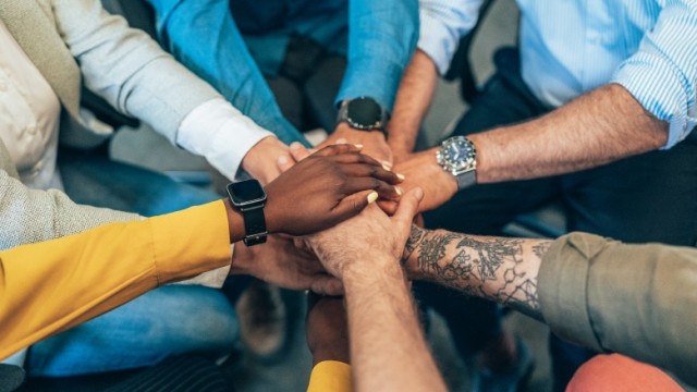 Nine people with hands in together as a team.
