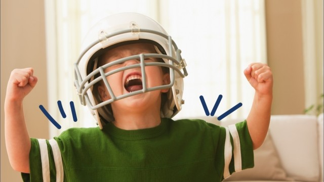 Little boy in an oversized football helmet shows his muscles and yells with excitement. 