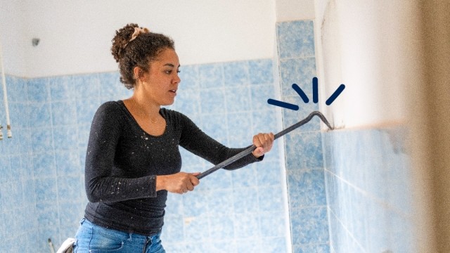 Woman uses a crowbar to remove tiles from a wall