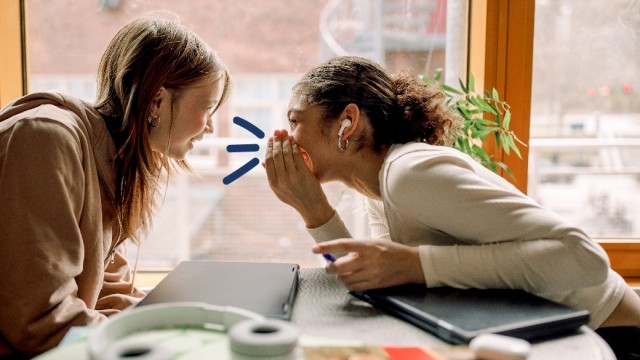 Two girls whisper to each other