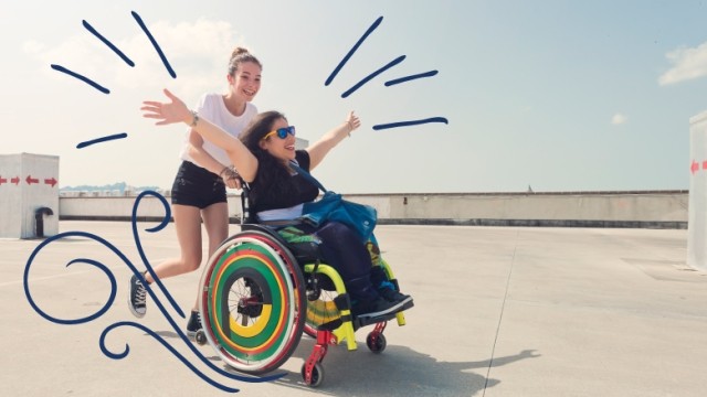 Teenage girl pushing friend in wheelchair with sunglasses on along the sunny beach sidewalk