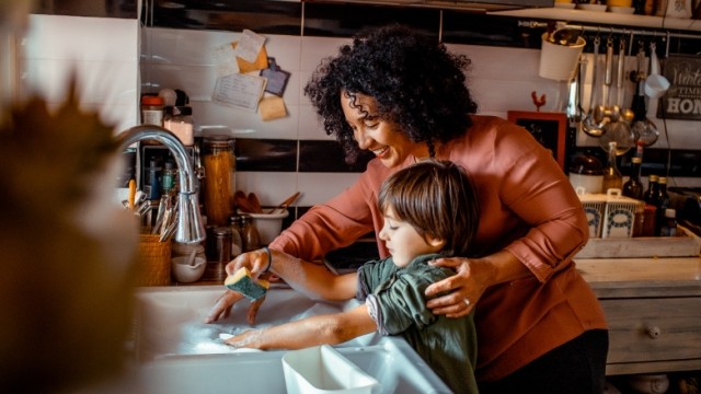 Mother with curly hair and son at home washing dishes in the sink