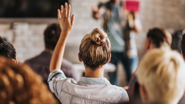 Girl with blonde hair in bun hairstyle raising hand.