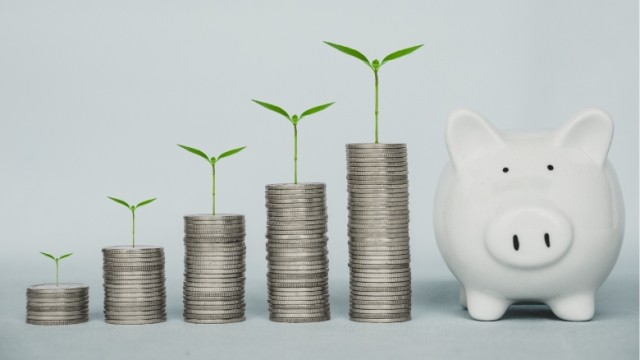 Five stacks of quarters growing taller with plants on top and white piggy bank.