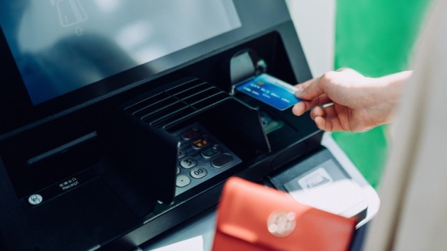 Person with red wallet inserting credit card into an Automated Teller Machine (ATM).