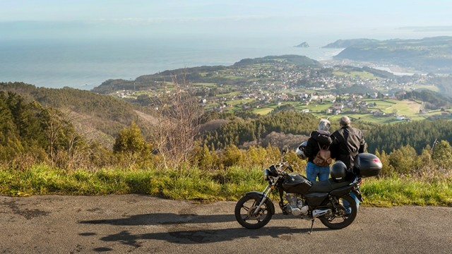 Motorcycle parked and couple overlooking the view of the ocean.