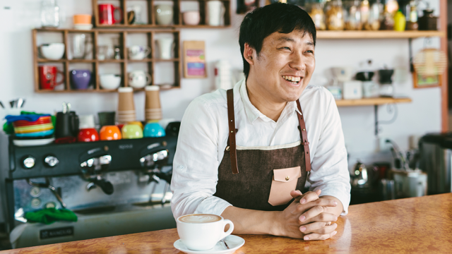 Asian man behind counter at his coffee shop