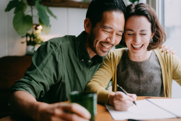 Two joyful partners reviewing finances at the kitchen table.
