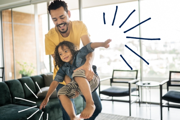Father holding child pretend flying like an airplane in home living room.