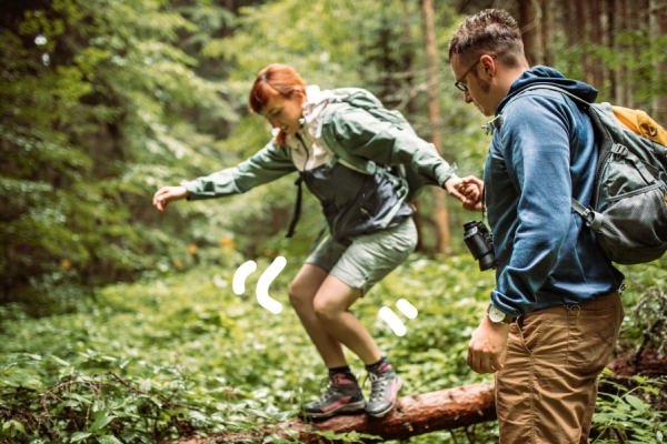 A man and a woman hike in a forested area with backpacks. 
