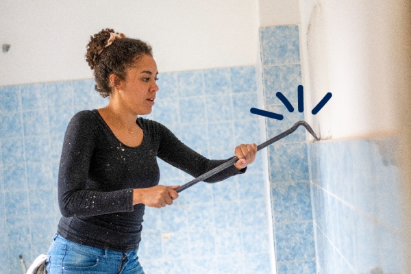 Woman uses a crowbar to remove tiles from a wall