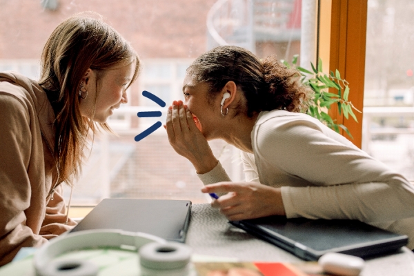 Two girls whisper to each other 