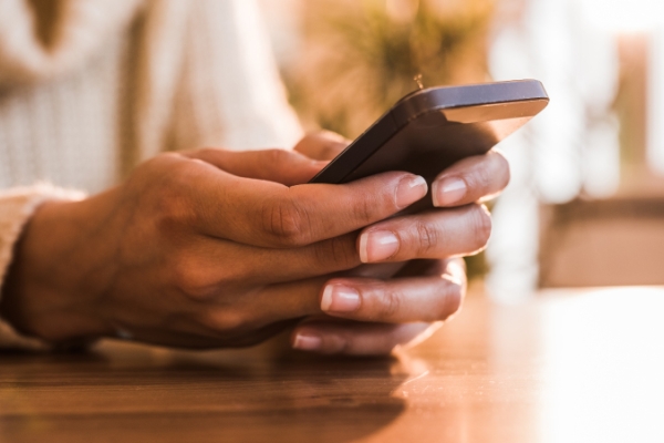 Two hands holding a cellphone on table.