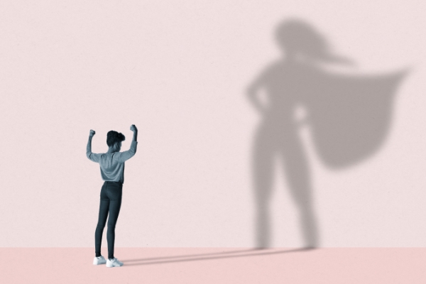 Person flexing muscles with superhero shadow casted on a wall