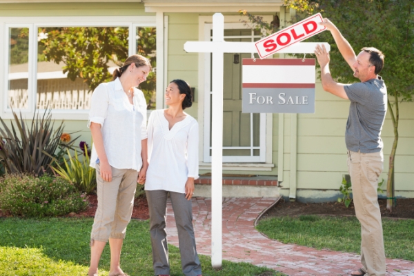 Partners with real estate agent in front of a home with a âSOLDâ sign.