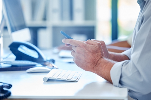 Personâs hands at a desk looking at a mobile phone.