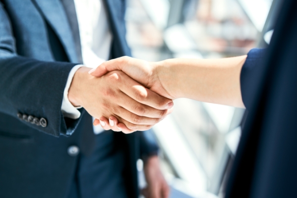 Two individuals in navy blue business suits shaking hands.