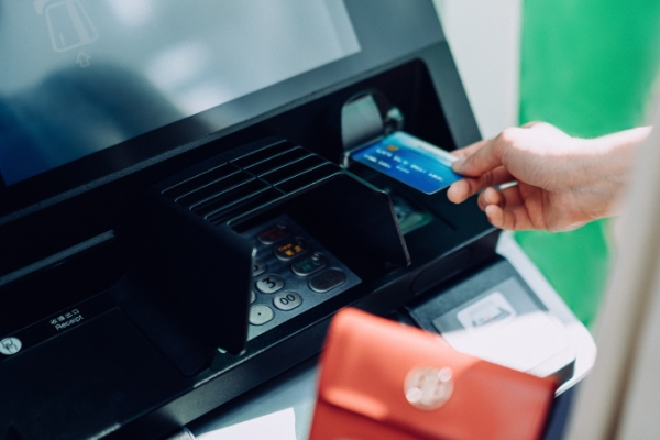 Person with red wallet inserting credit card into an Automated Teller Machine (ATM).