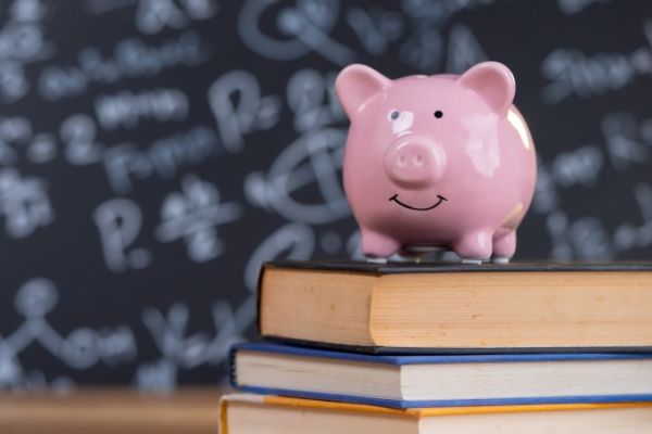 A pink piggy bank on top of a stack of three books with a school chalkboard in the background