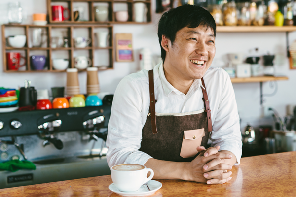 Asian man behind counter at his coffee shop