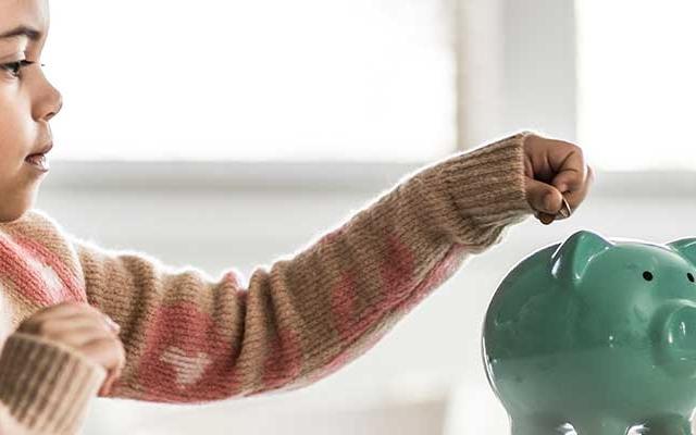 girl putting coin into piggy bank