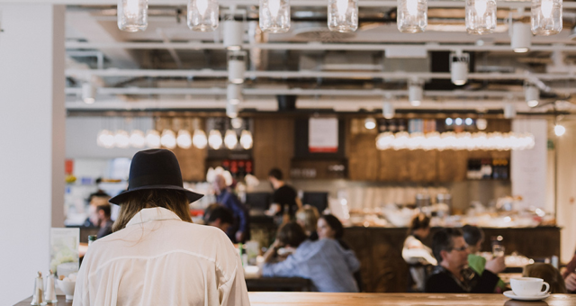 Man standing with his back turned in a cafe wearing a black hat