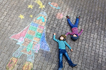 Kids laying next to a chalk rocketship on the sidewalk